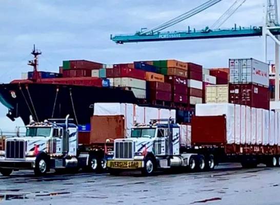 shipping containers on a ship with two flatbed diesel trucks in front